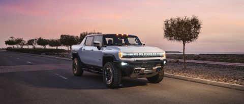 Interstellar White GMC HUMMER EV on a coastal road at sunset.