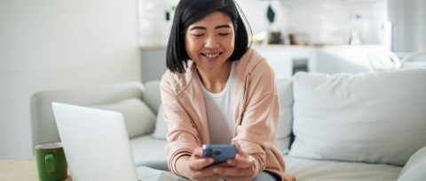 Smiling young woman checking credit score on her phone while applying for auto financing.