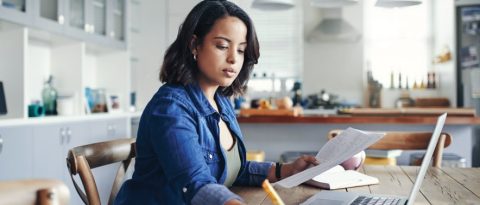 Woman creating a line-item budget at her kitchen table.