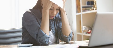 Woman worrying over money management mistakes in front of computer.