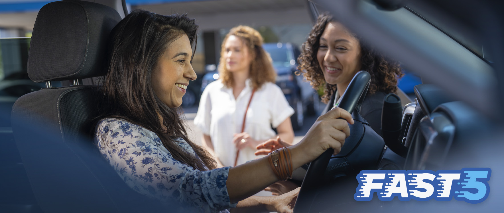 Mujer sonriente preparándose para conducir un vehículo GM nuevo fuera del estacionamiento, con el logotipo de Fast 5 superpuesto.