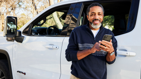 Smiling african american man standing next to a while Chevrolet truck holding his phone.